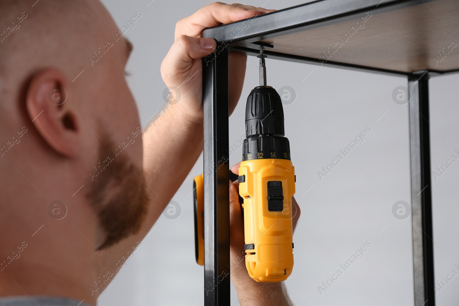 Photo of Man with electric screwdriver assembling furniture indoors, closeup