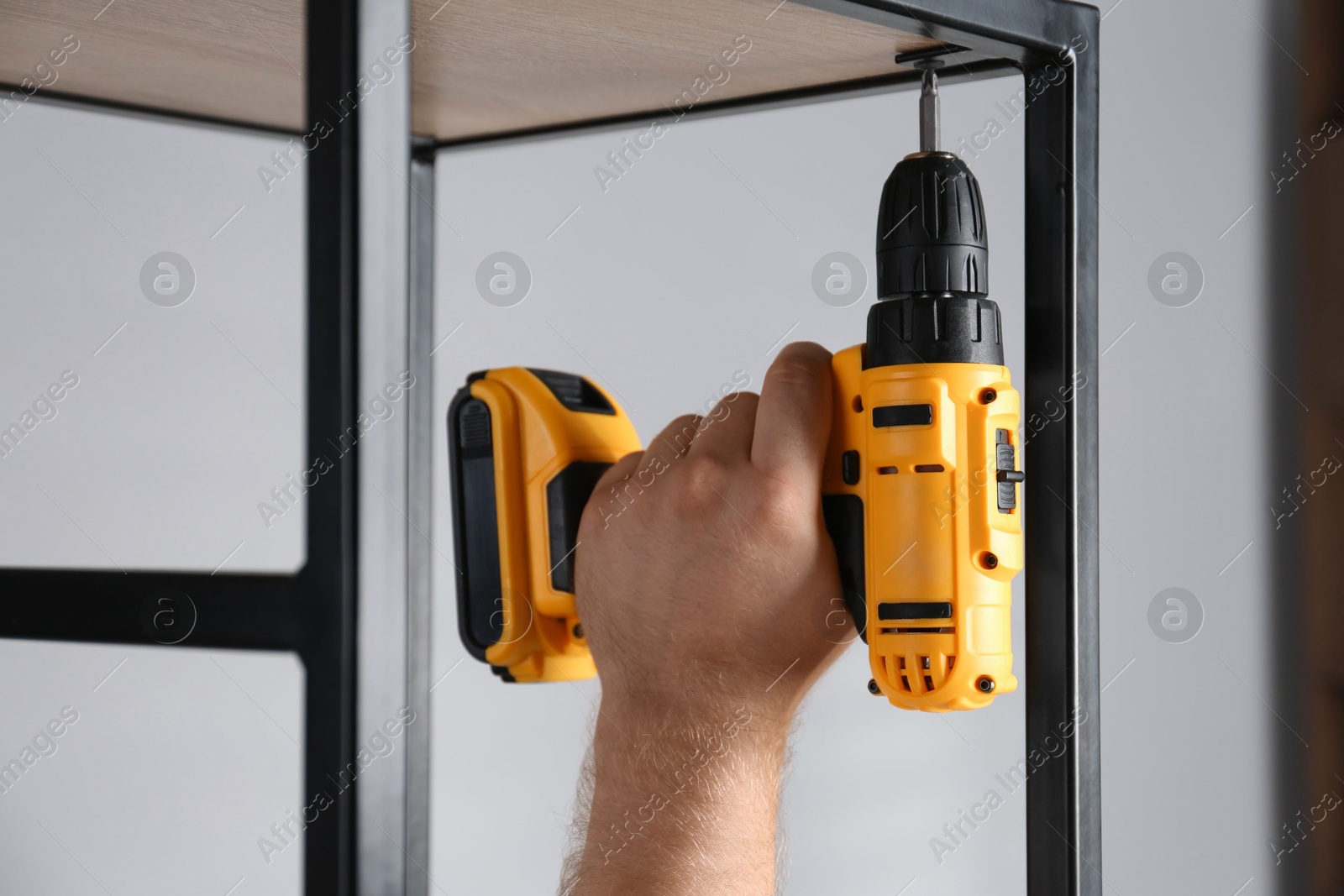 Photo of Man with electric screwdriver assembling furniture indoors, closeup