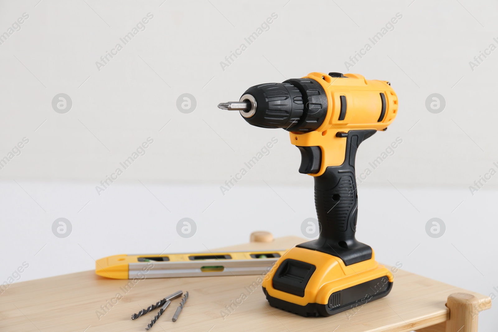 Photo of Electric screwdriver, drill bits and building level on wooden table against light background. Space for text