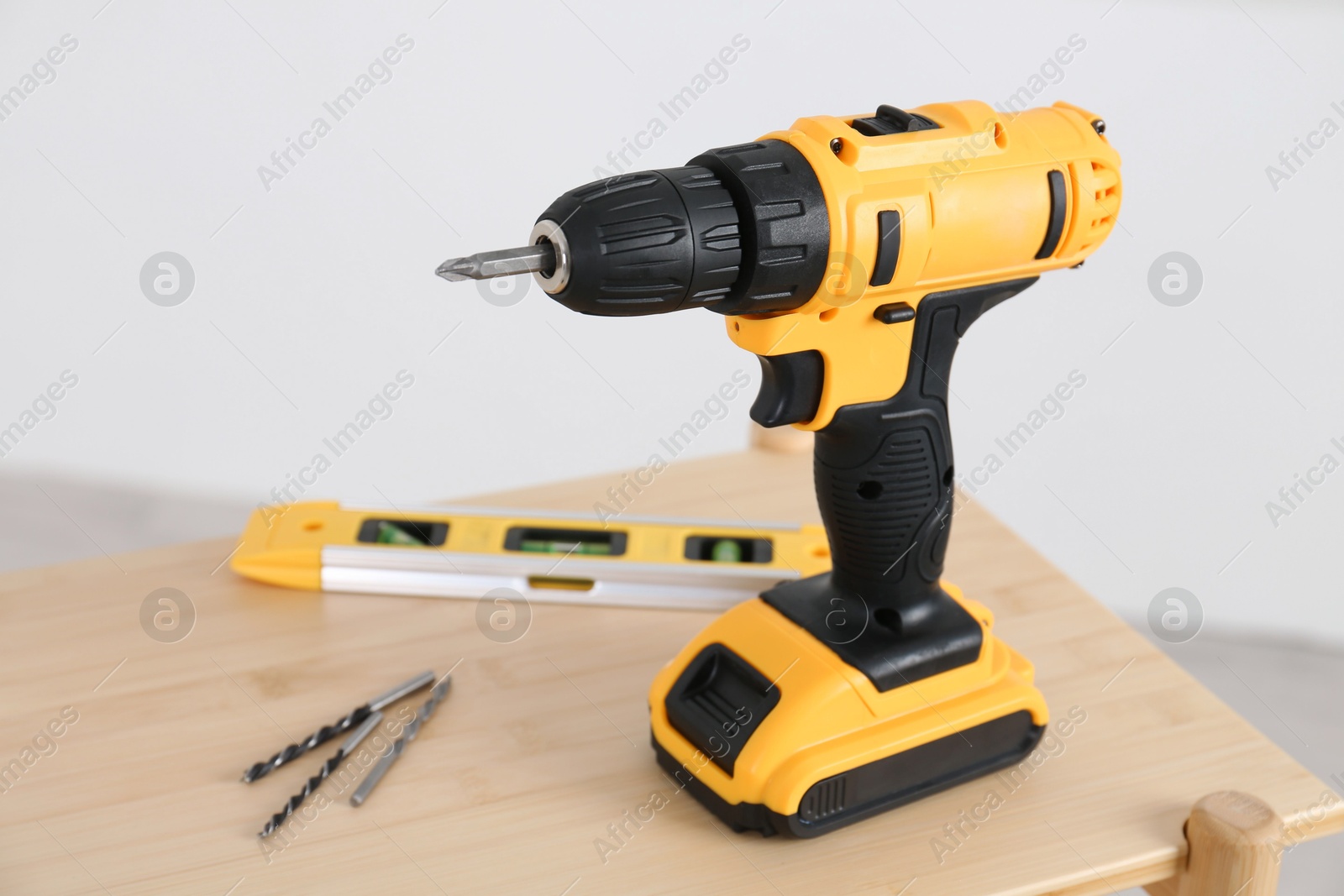 Photo of Electric screwdriver, drill bits and building level on wooden table against light background, closeup