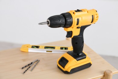 Electric screwdriver, drill bits and building level on wooden table against light background, closeup