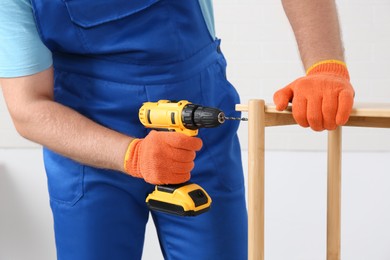 Photo of Worker with electric screwdriver assembling furniture indoors, closeup