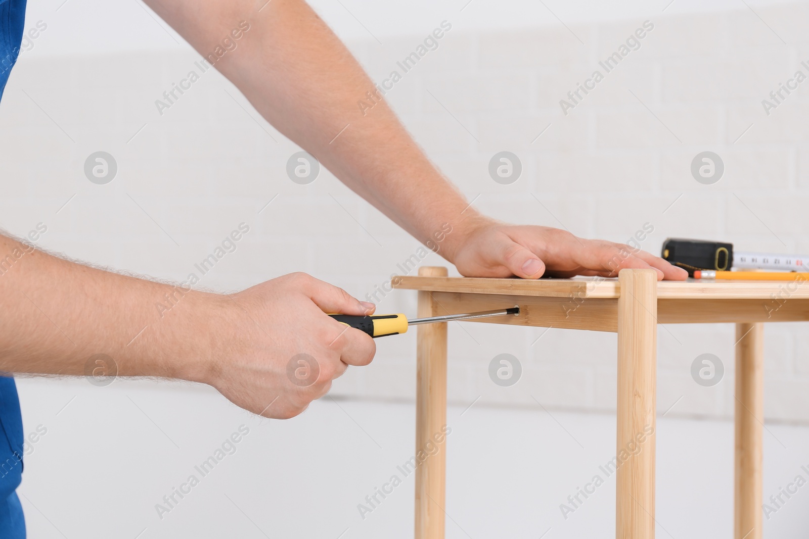 Photo of Worker with screwdriver assembling furniture indoors, closeup