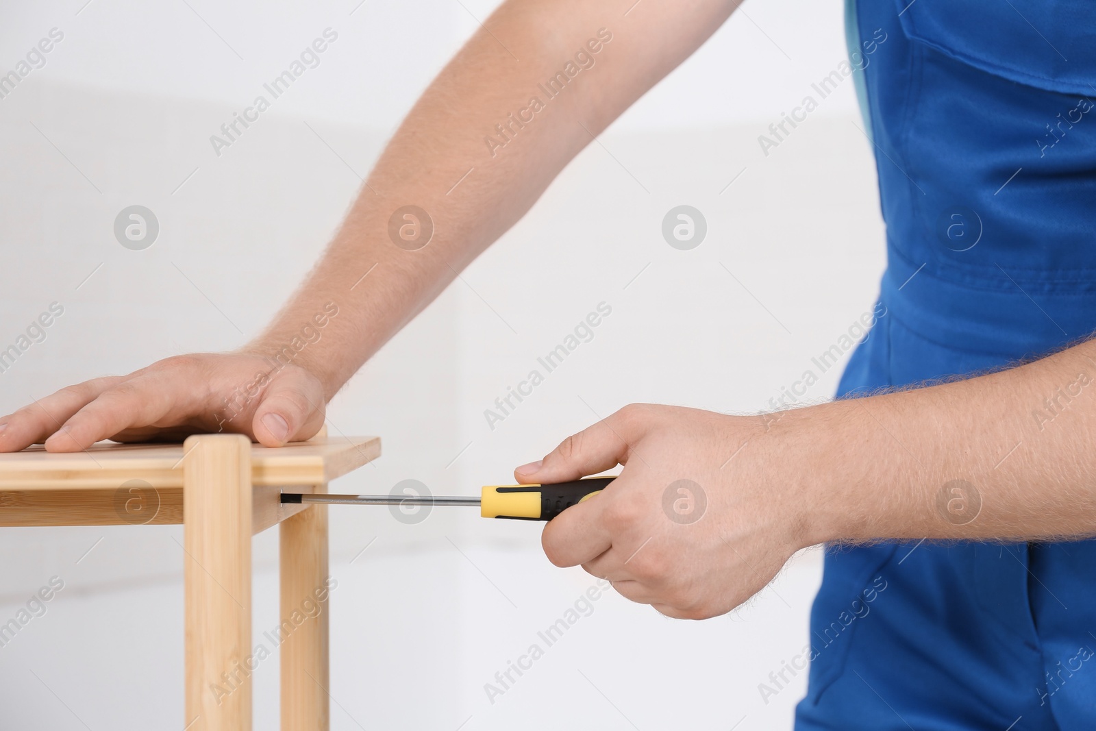 Photo of Worker with screwdriver assembling furniture indoors, closeup