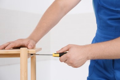 Photo of Worker with screwdriver assembling furniture indoors, closeup