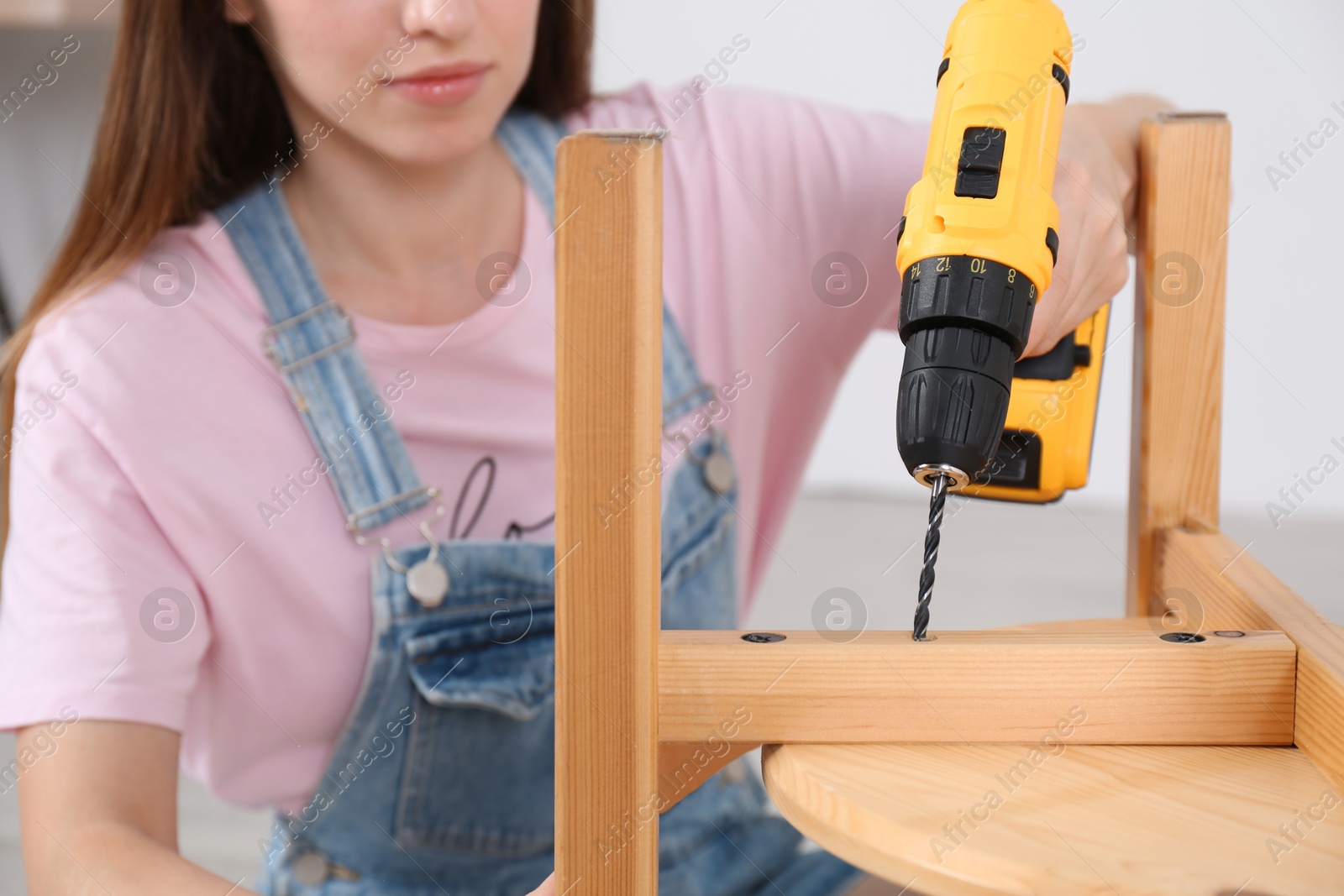 Photo of Woman with electric screwdriver assembling furniture indoors, closeup