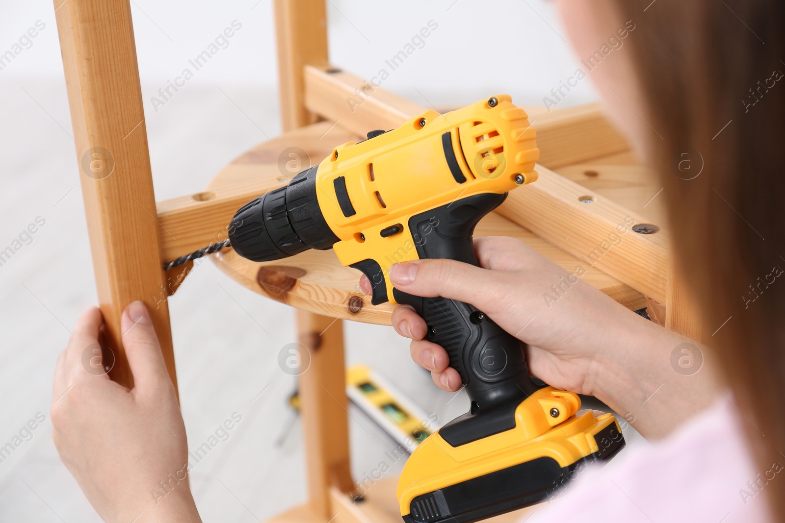 Photo of Woman with electric screwdriver assembling furniture indoors, closeup