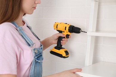 Woman with electric screwdriver assembling furniture indoors, closeup