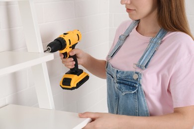 Photo of Woman with electric screwdriver assembling furniture indoors, closeup