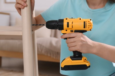 Woman with electric screwdriver assembling furniture in room, closeup