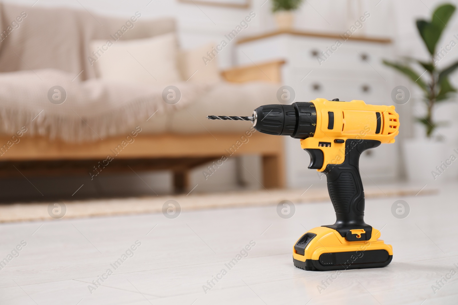 Photo of Cordless electric screwdriver on floor at home. Space for text