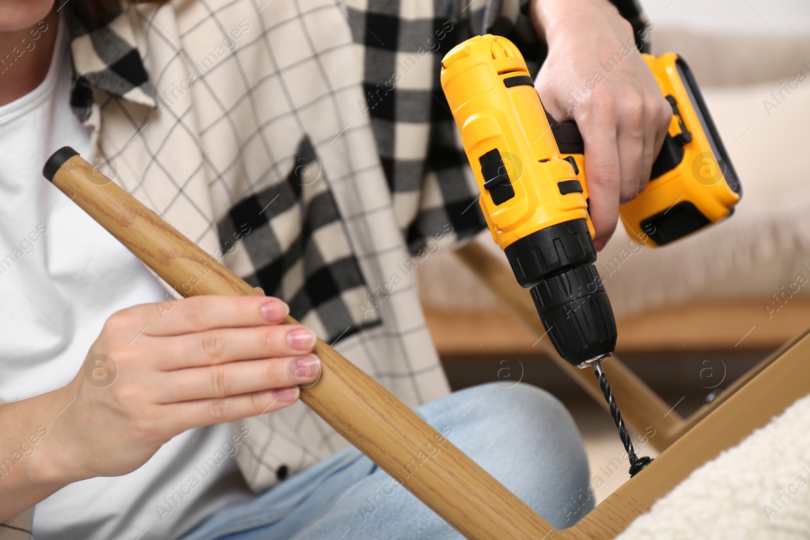 Photo of Woman with electric screwdriver assembling armchair in room, closeup