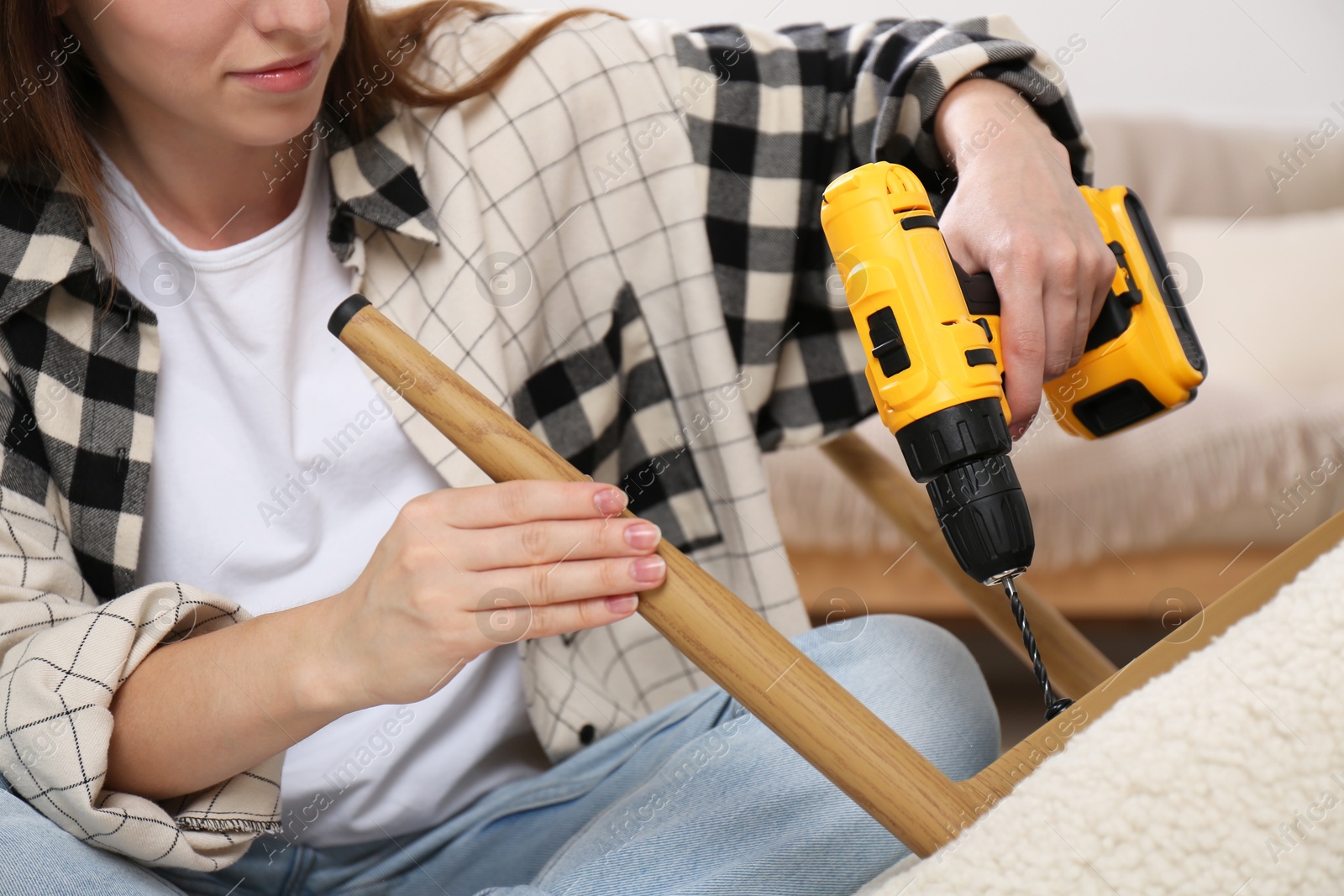 Photo of Woman with electric screwdriver assembling armchair in room, closeup