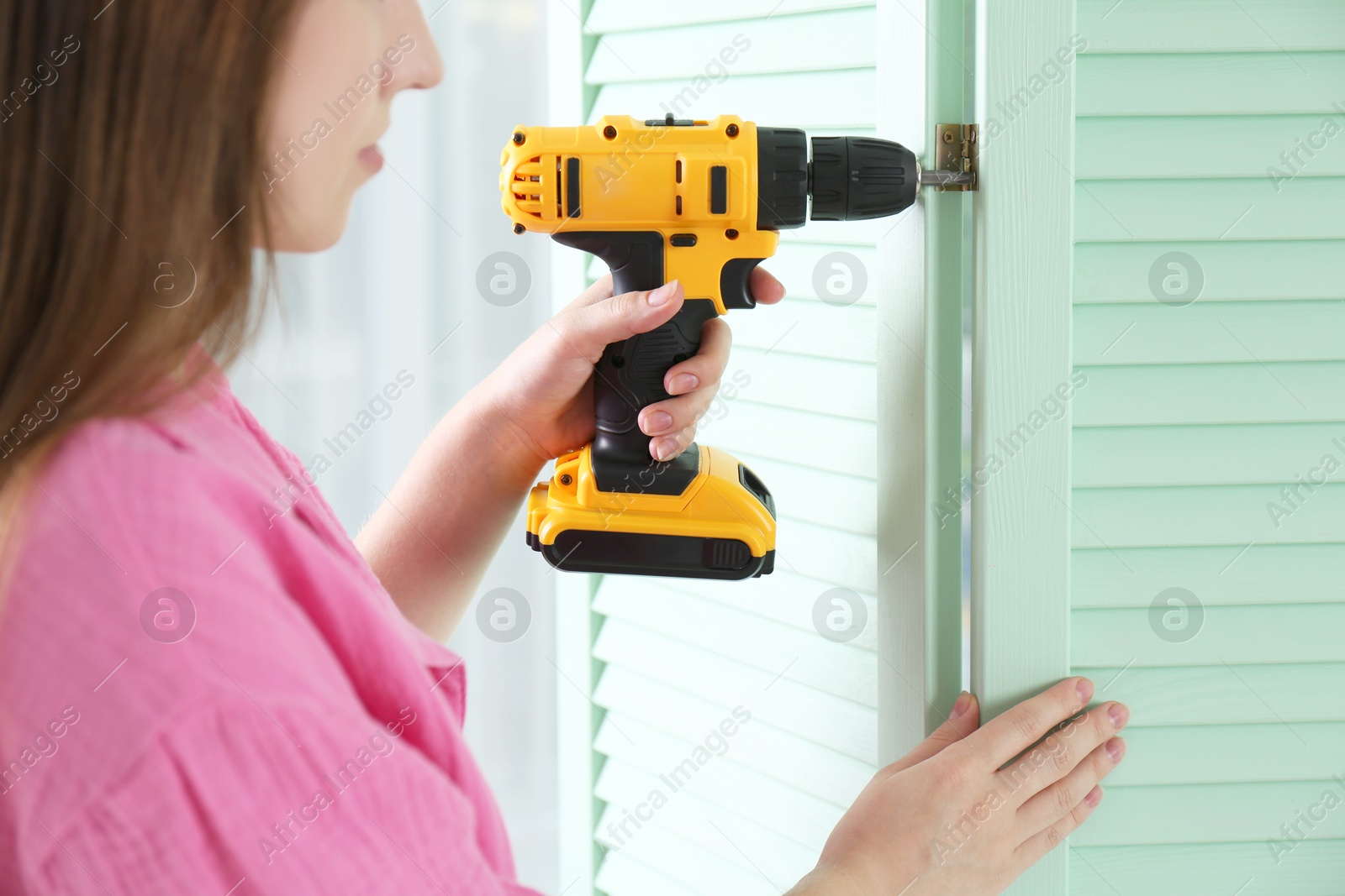 Photo of Woman with electric screwdriver assembling folding screen at home, closeup