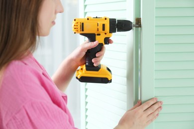 Woman with electric screwdriver assembling folding screen at home, closeup