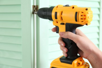 Photo of Woman with electric screwdriver assembling folding screen at home, closeup