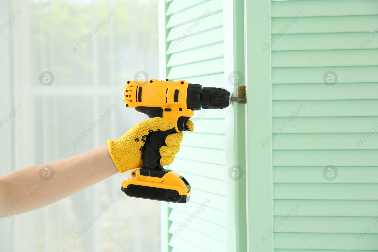 Photo of Woman with electric screwdriver assembling folding screen at home, closeup