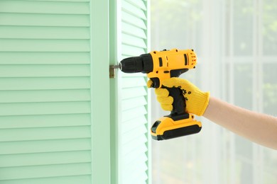 Photo of Woman with electric screwdriver assembling folding screen at home, closeup