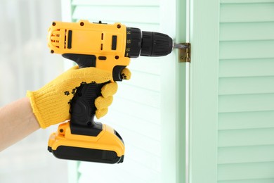 Photo of Woman with electric screwdriver assembling folding screen at home, closeup