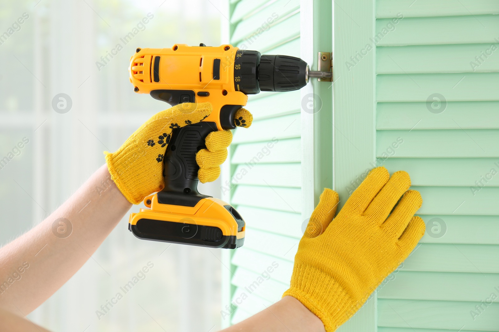 Photo of Woman with electric screwdriver assembling folding screen at home, closeup