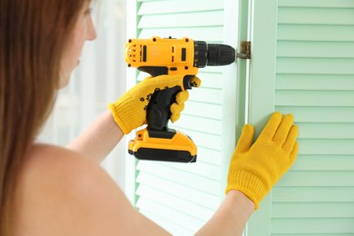 Woman with electric screwdriver assembling folding screen indoors