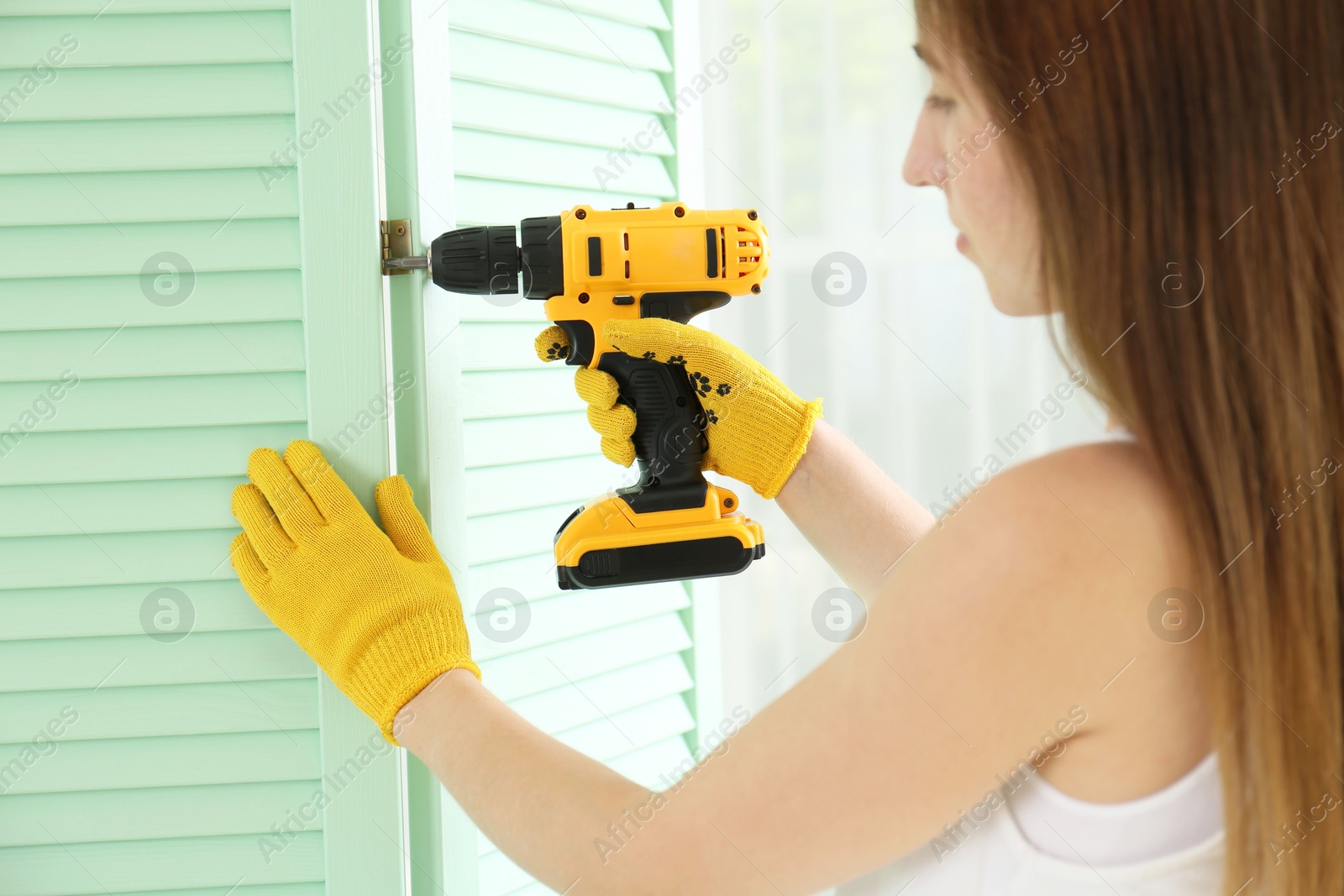 Photo of Woman with electric screwdriver assembling folding screen indoors