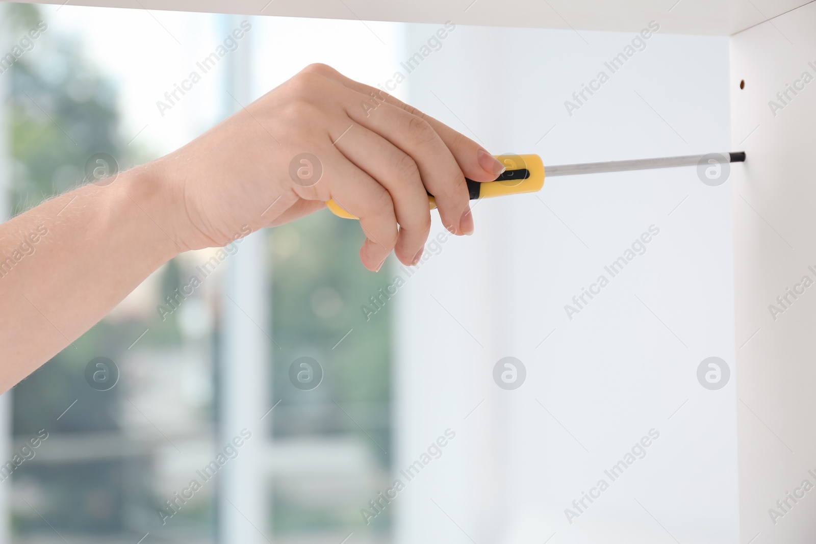 Photo of Woman with screwdriver assembling furniture indoors, closeup