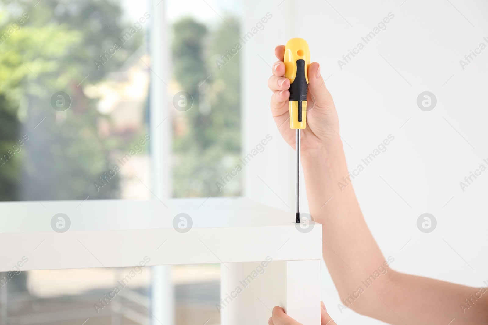 Photo of Woman with screwdriver assembling furniture indoors, closeup