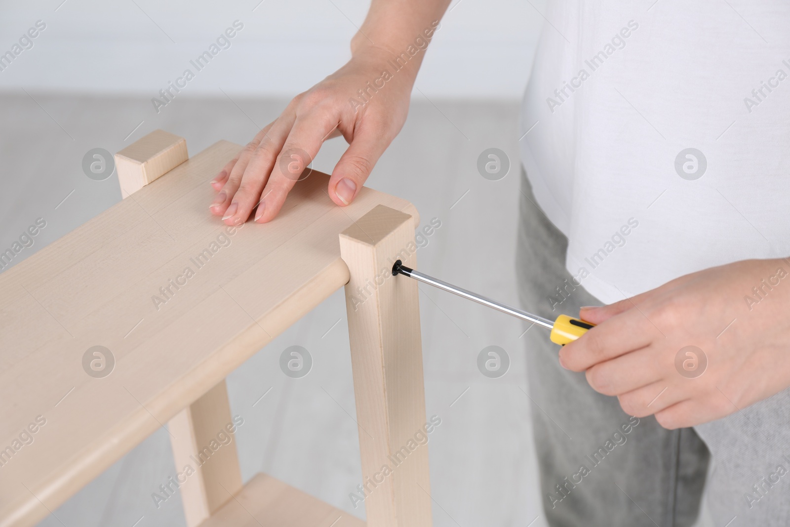 Photo of Woman with screwdriver assembling furniture indoors, closeup