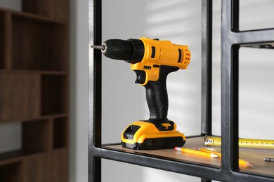 Photo of Electric screwdriver, pencils and tape measure on shelving unit indoors