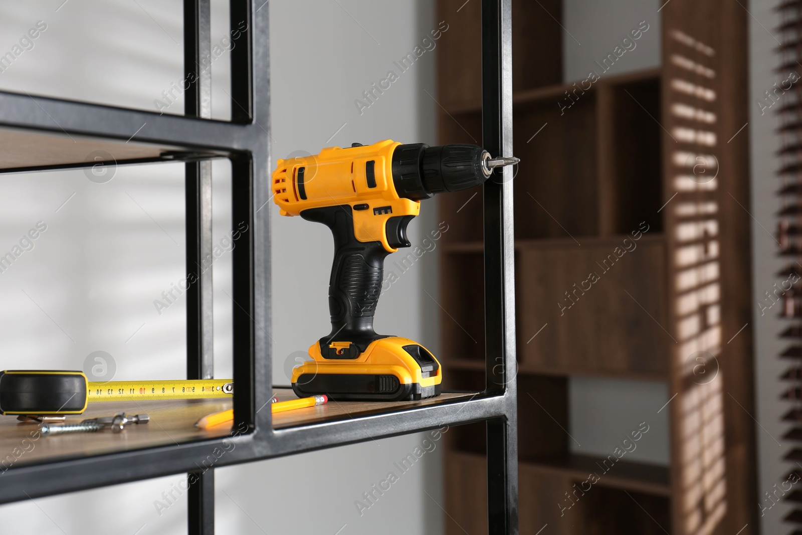 Photo of Electric screwdriver, pencils, drill bits and tape measure on shelving unit indoors