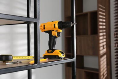 Photo of Electric screwdriver, pencils, drill bits and tape measure on shelving unit indoors