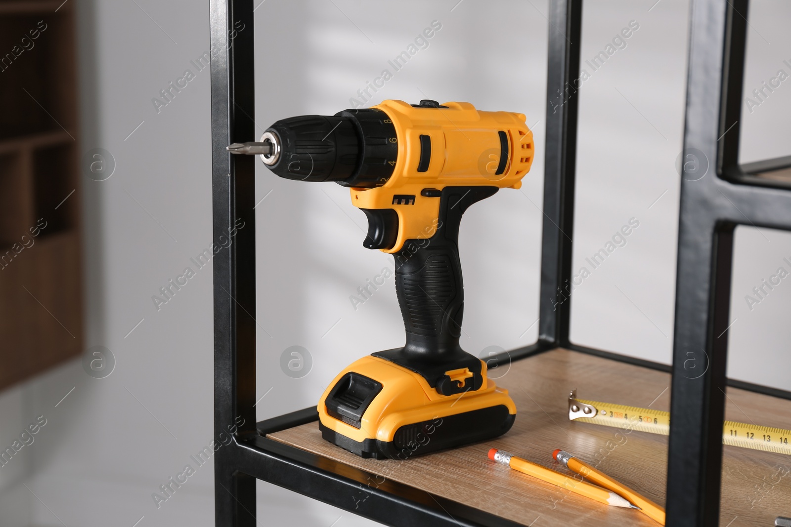 Photo of Electric screwdriver, pencils and tape measure on shelving unit indoors