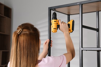 Woman with electric screwdriver assembling shelving unit in room