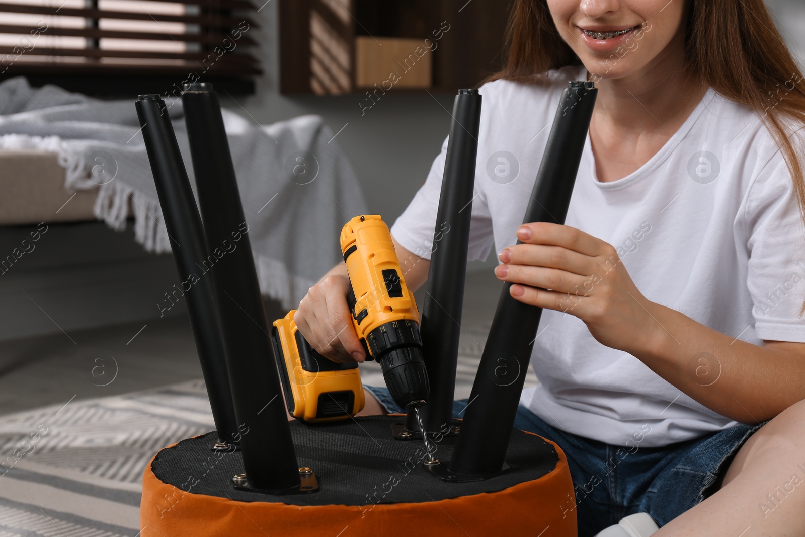 Photo of Woman with electric screwdriver assembling pouf at home, closeup