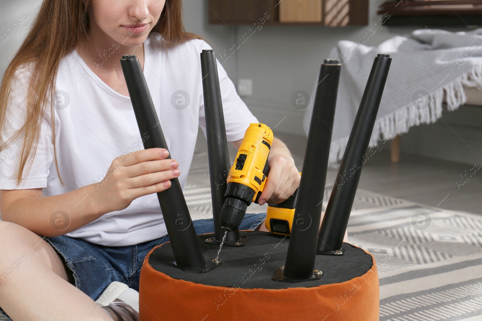 Photo of Woman with electric screwdriver assembling pouf at home, closeup