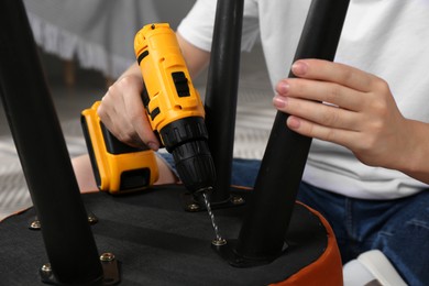 Photo of Woman with electric screwdriver assembling pouf at home, closeup