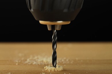 Photo of Drilling hole in wooden plank on black background, closeup