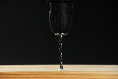 Photo of Drilling hole in wooden plank on black background, closeup