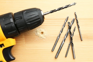 Photo of Cordless electric drill, and bits on holed wooden surface, flat lay