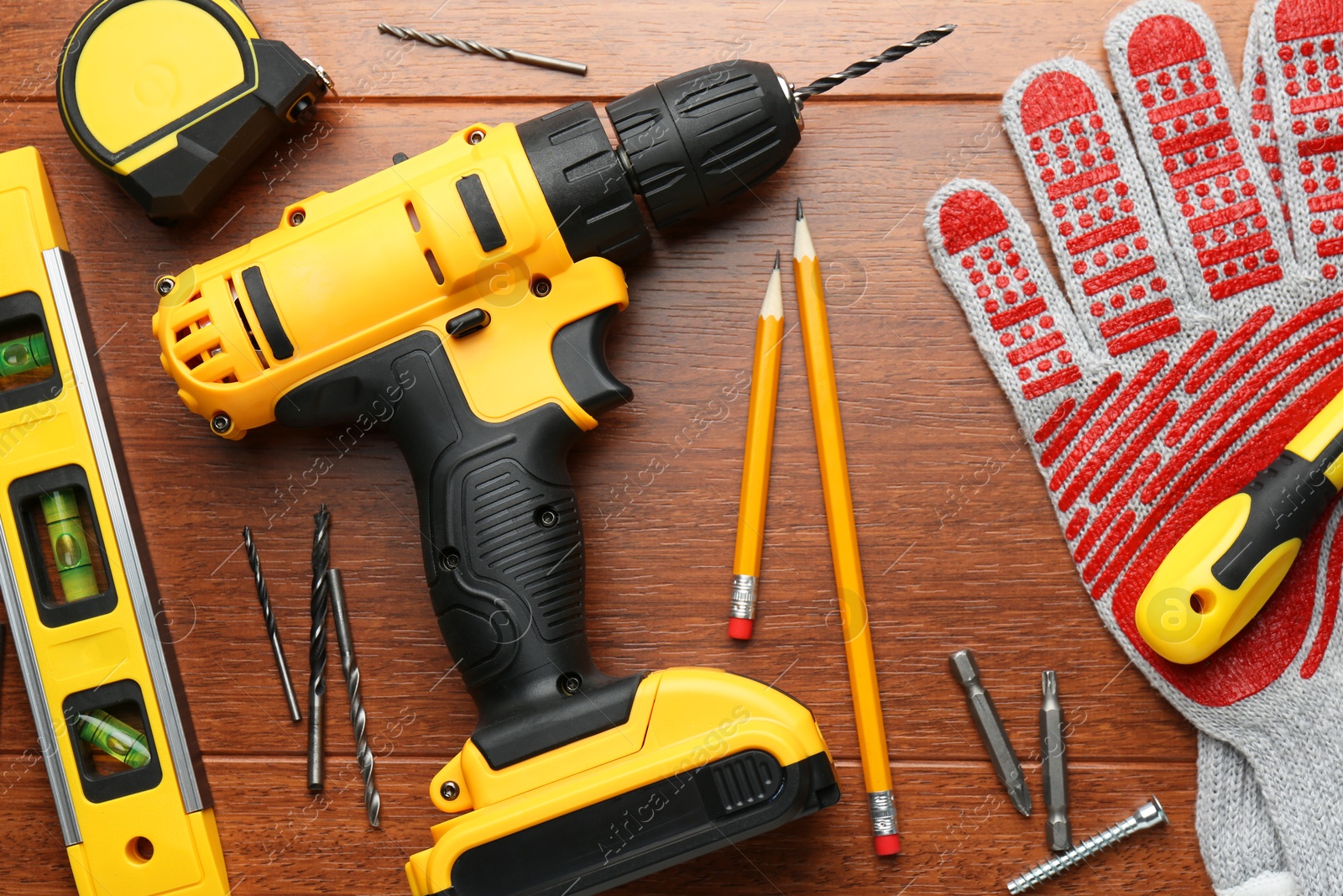 Photo of Cordless electric drill, gloves, pencils and construction tools on wooden table, flat lay