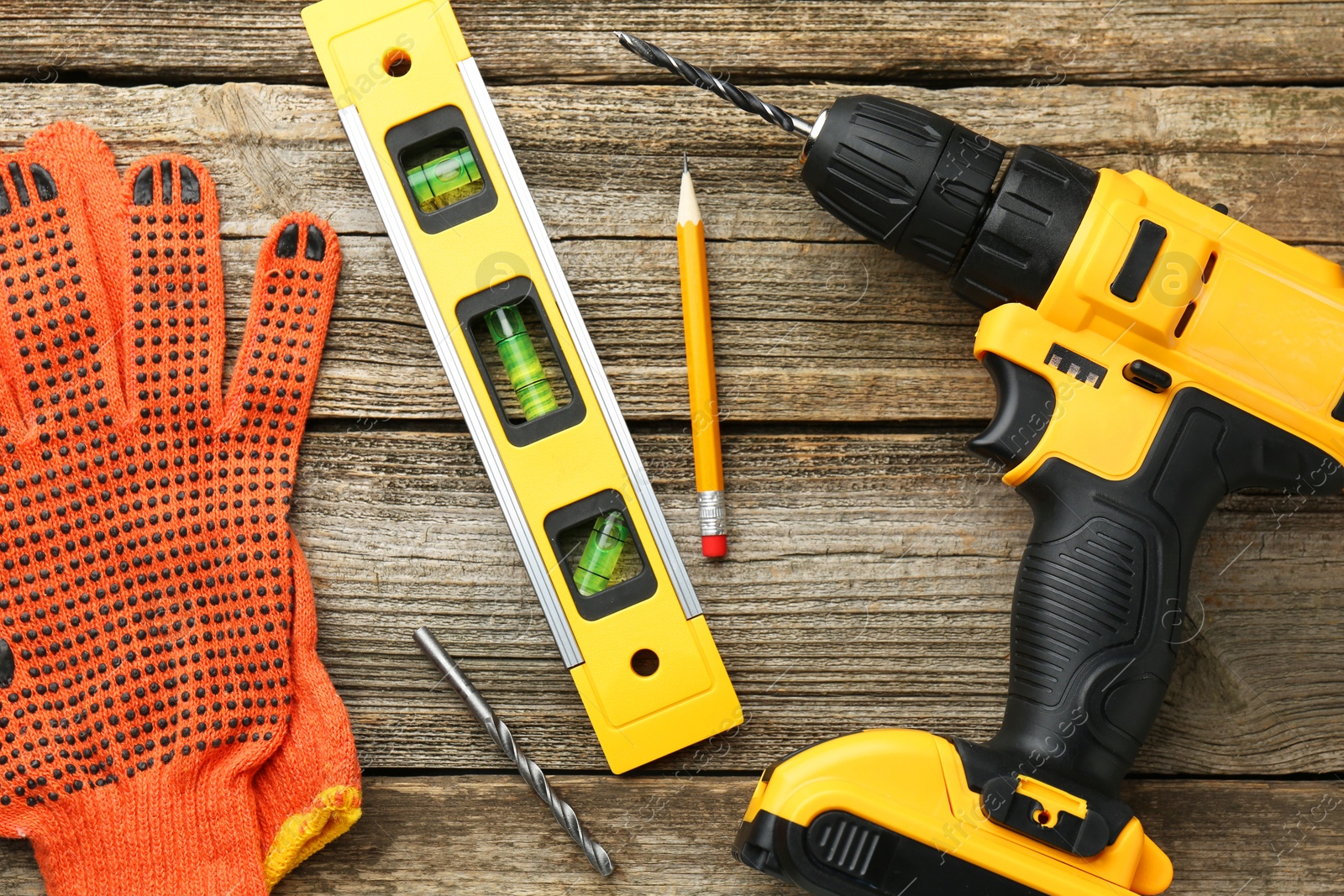 Photo of Cordless electric drill, gloves, pencil, bits and building level on wooden table, flat lay