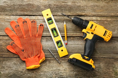 Photo of Cordless electric drill, gloves, pencil, bits and building level on wooden table, flat lay