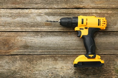 Photo of Cordless electric drill on wooden table, top view. Space for text