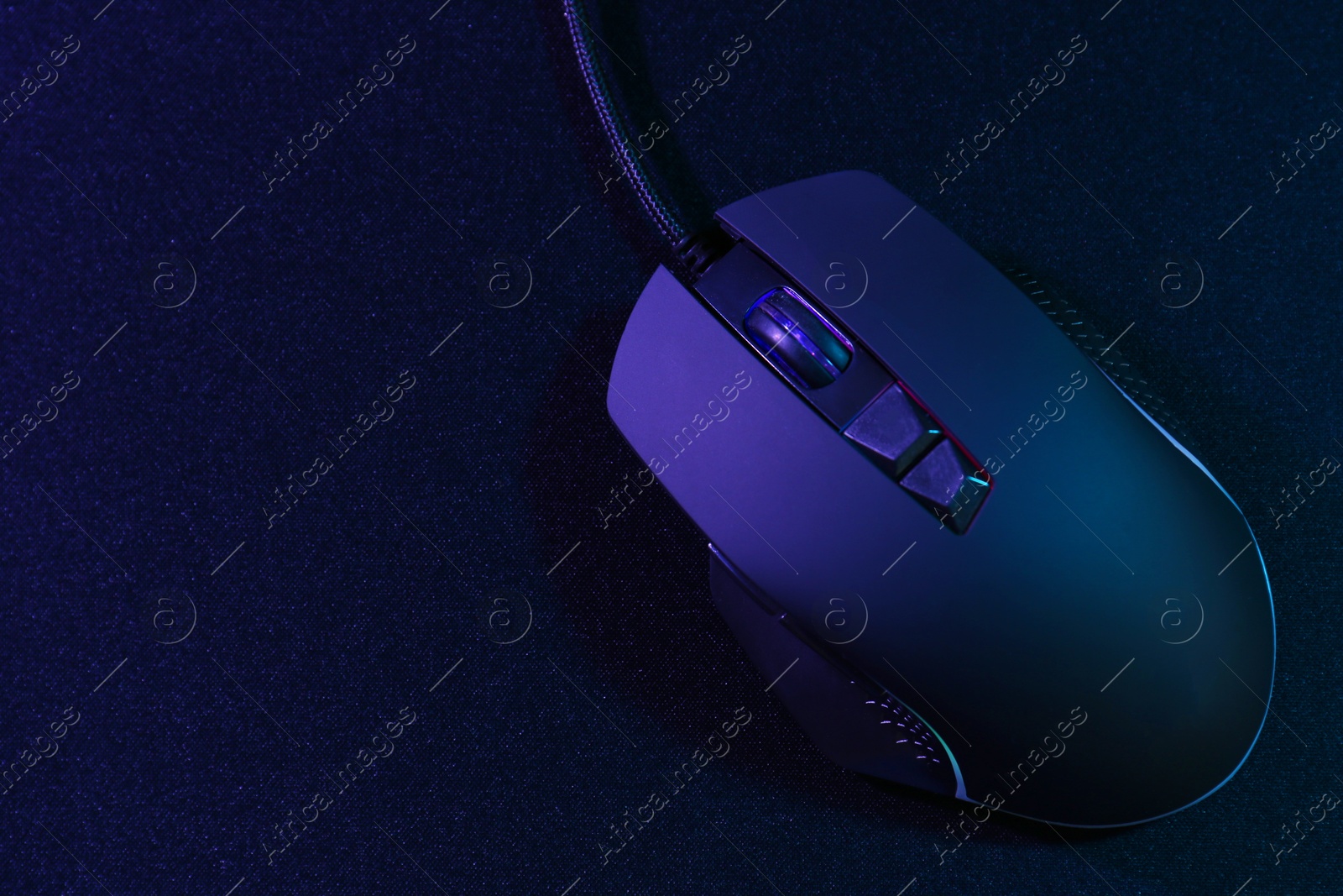 Photo of Black computer mouse and mousepad in neon lights, top view. Space for text