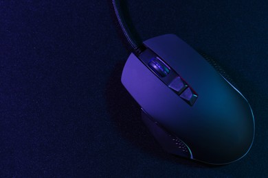 Photo of Black computer mouse and mousepad in neon lights, top view. Space for text