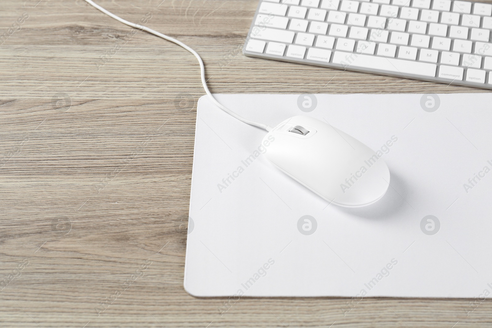 Photo of White computer mouse with mousepad and keyboard on wooden table