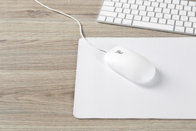 Photo of White computer mouse with mousepad and keyboard on wooden table