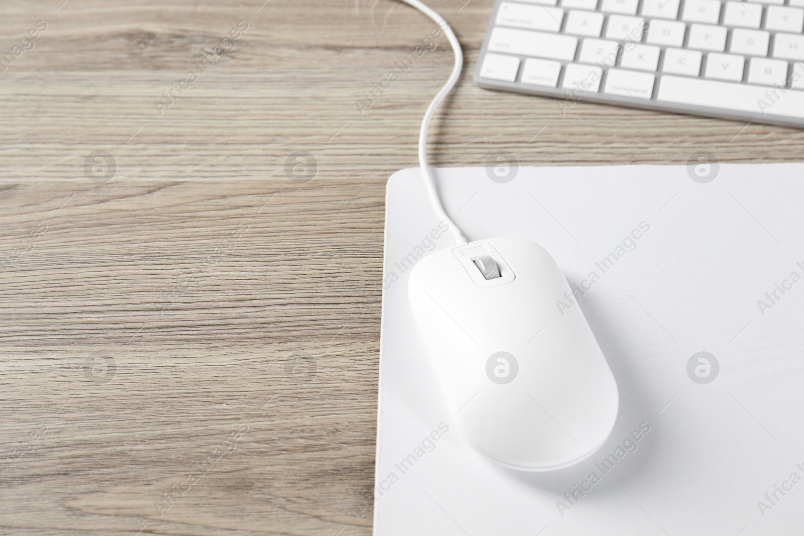 Photo of White computer mouse with mousepad and keyboard on wooden table