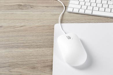 Photo of White computer mouse with mousepad and keyboard on wooden table